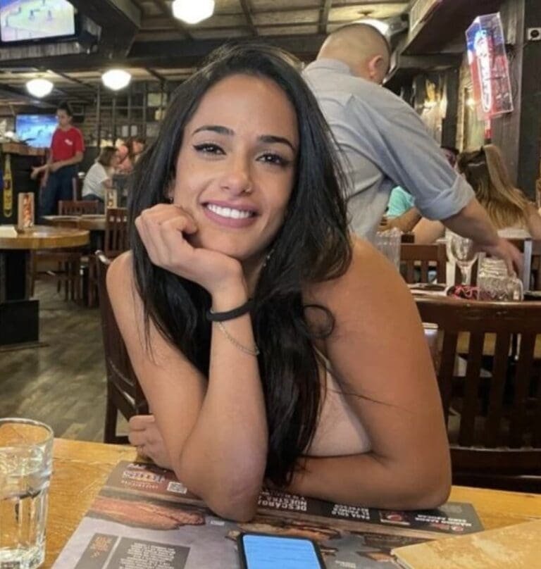 A young woman smiling warmly, seated at a table in a cozy pub, exuding a sense of joy and casual ease.