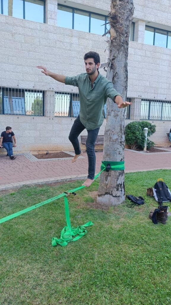 A young man balances on a slackline tied between trees, focused and at peace.