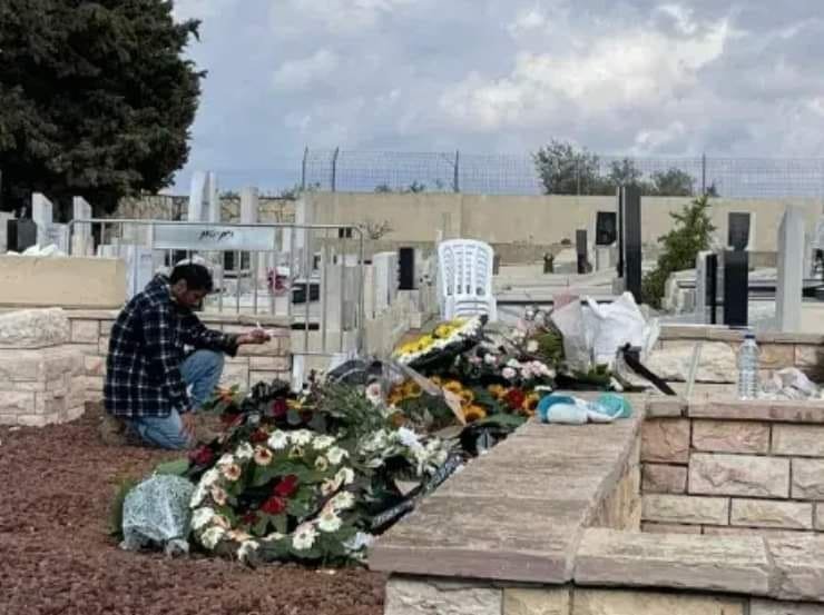 A solitary man kneeling at a grave adorned with flowers, holding a ring in a poignant personal moment of loss.