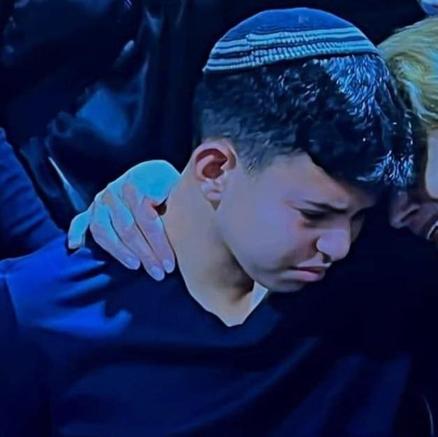 A grieving young boy wearing a yarmulke is being comforted.