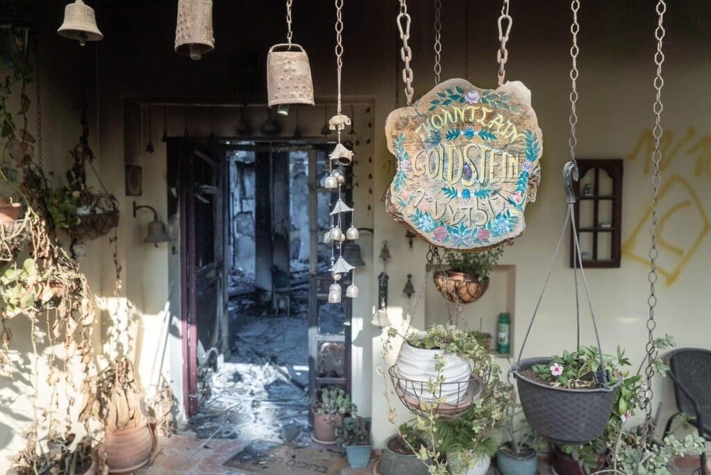 A poignant juxtaposition of a burnt interior and a serene porch with wind chimes and a sign reading "Goldstein."