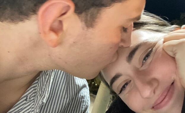 A tender moment of a young man kissing the forehead of a smiling young woman.