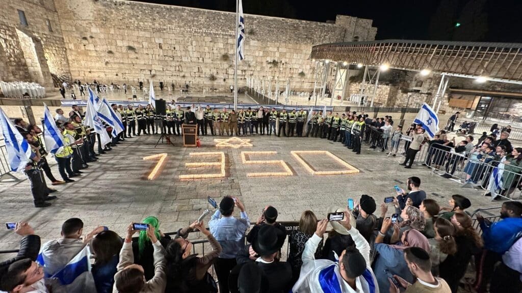 A solemn vigil at the Western Wall with 1,350 candles illuminating the night, each representing a soul lost in the "Iron Swords" war