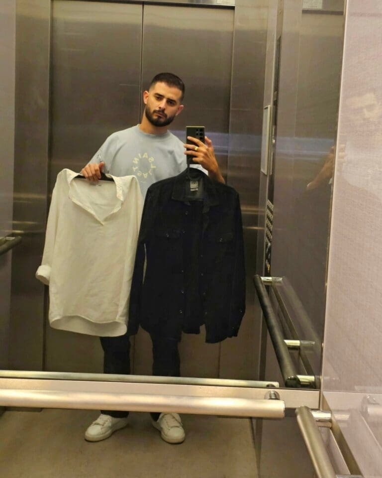 A young man in an elevator, poised between moments of sorrow and celebration, holding two shirts.