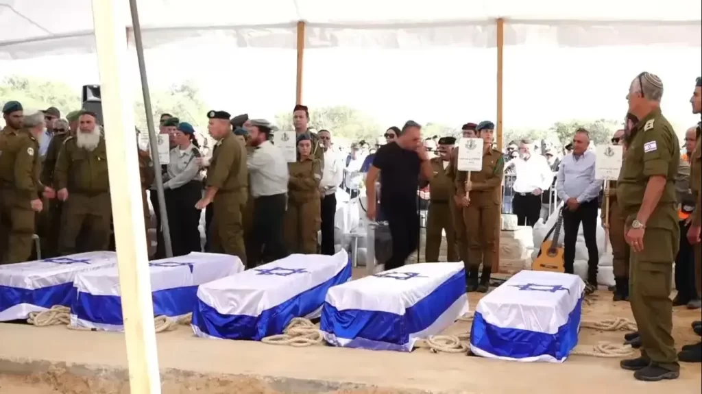 A solemn gathering at a funeral with five caskets draped in the flag of Israel.