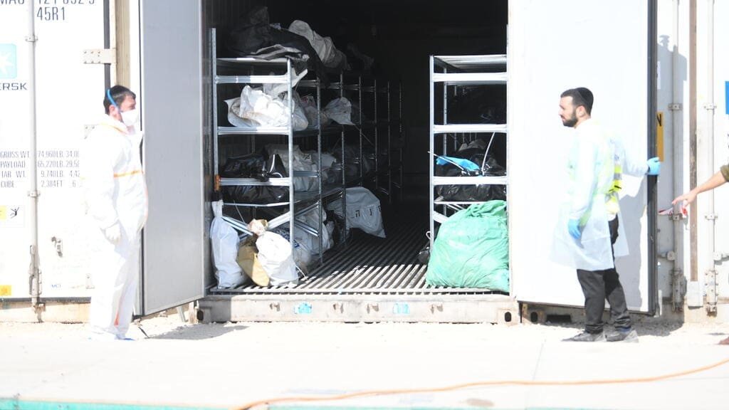 Two individuals in protective gear stand near an open shipping container filled with black bags.