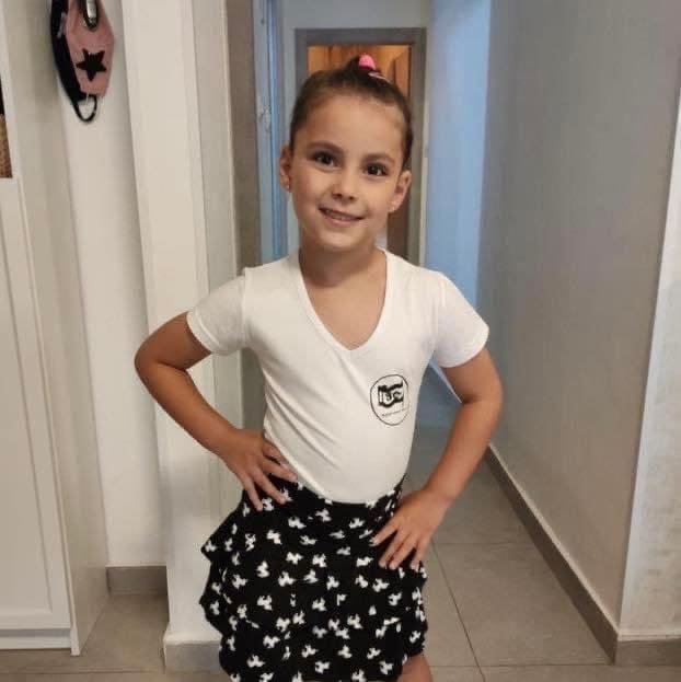 A young girl in a ballet outfit, posing for the camera with a bright smile, unaware of the tragic fate that awaits her due to a Hamas attack.