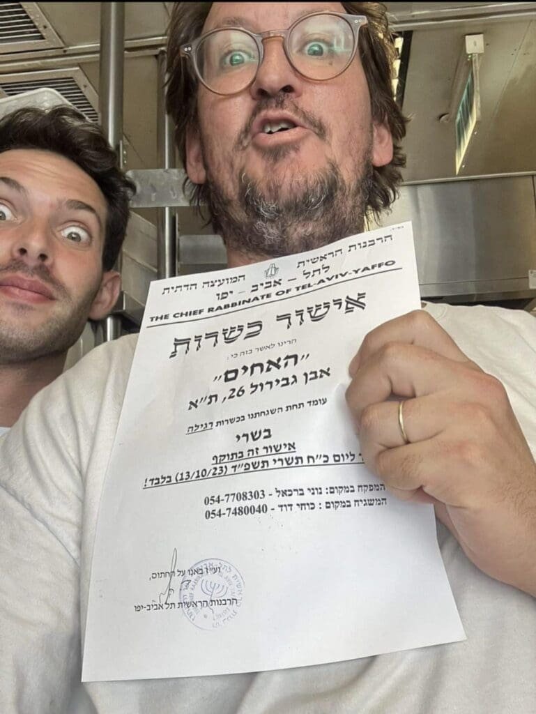 Two individuals holding a temporary kosher certificate issued by the Chief Rabbinate of Tel Aviv-Yafo.