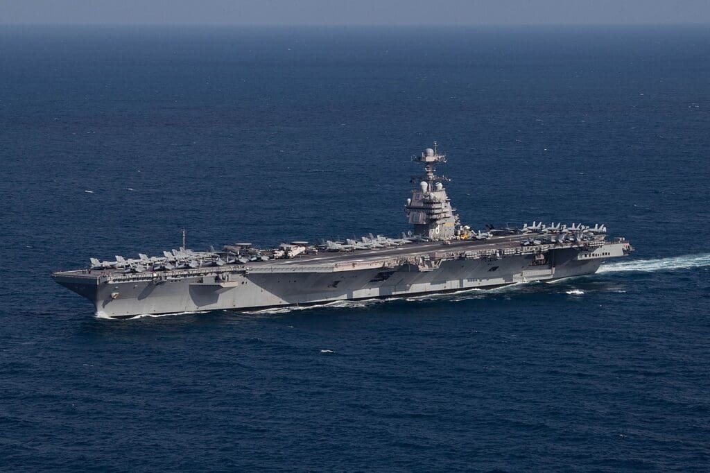 Aerial view of a Nimitz-class aircraft carrier with multiple military aircraft on deck at sea.